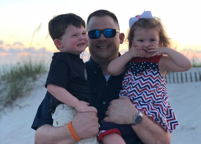 Andy Palys is holding James Palys and Kaitlyn Palys while standing on the beach.